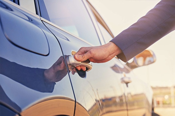 Close-up of a person in a suit opening the door of a black luxury car, representing a private transfer service.