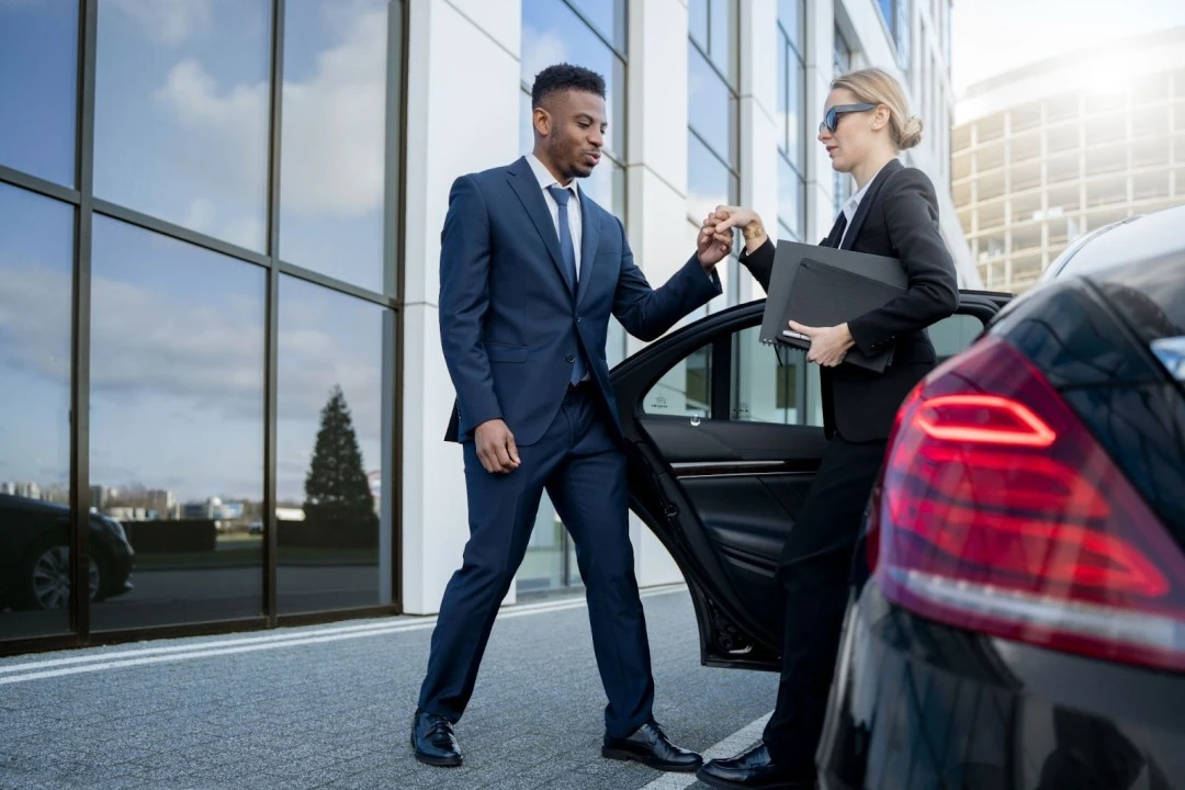 Chauffeur assisting a businesswoman into a luxury black car outside a modern office building.