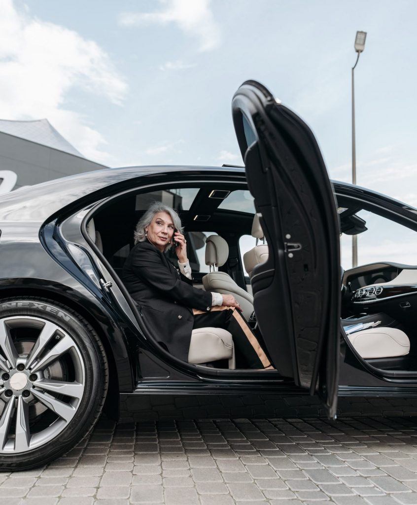 Businesswoman stepping out of a luxury car with a phone, symbolizing elegance and convenience in private transfers.