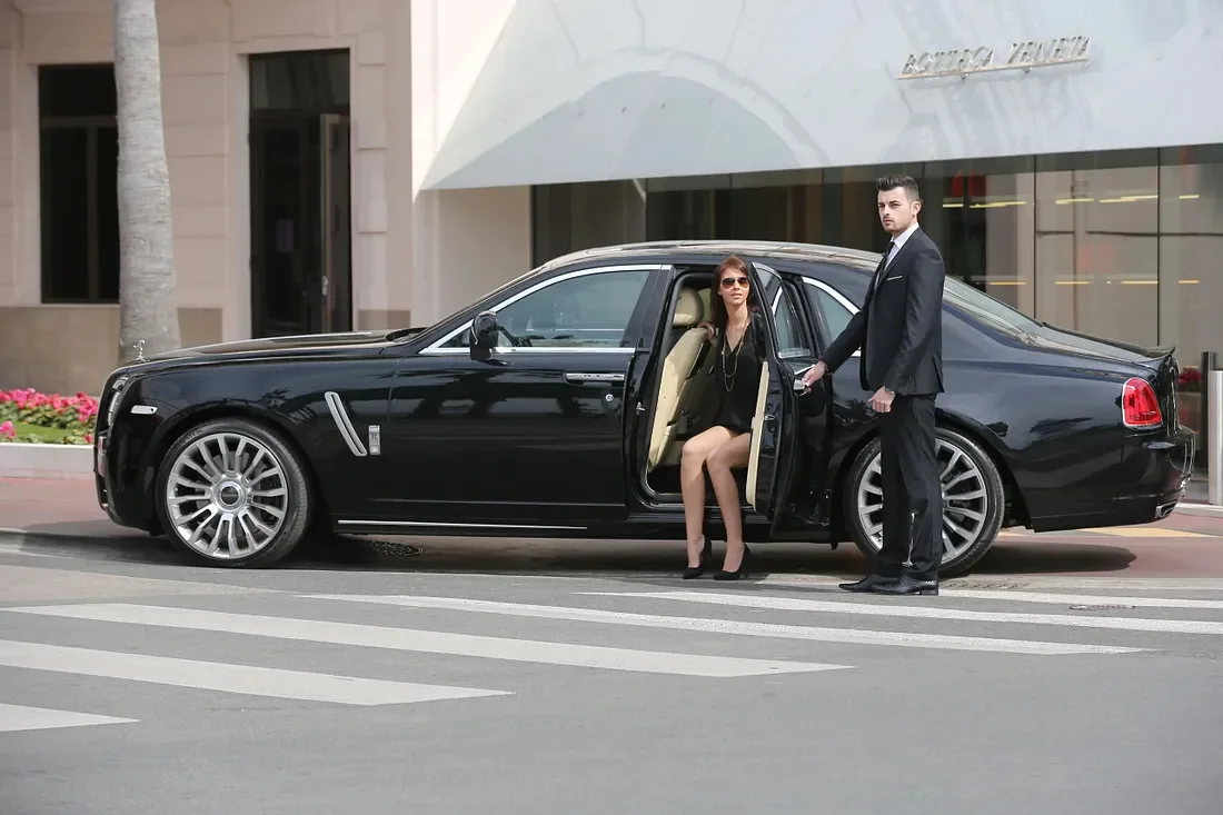 Chauffeur holding the door of a luxury black sedan for a stylish woman in sunglasses, symbolizing VIP chauffeur service.